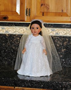 a doll wearing a white dress and veil on top of a kitchen counter with wooden cabinets