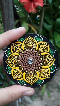 a hand holding a small decorative object in front of some flowers