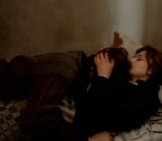 two people laying on a bed kissing each other