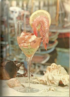 a glass filled with shrimp and garnish on top of a table next to shells