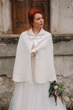 a woman in a white wedding dress and cape