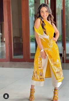 a woman standing in front of a building wearing yellow and white clothing with her hands on her hips