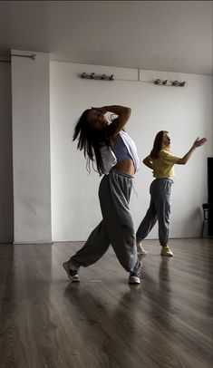 two young women are dancing in an empty room with wood flooring and white walls