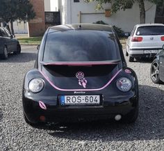 a black car with pink trim parked on gravel