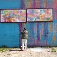 a man is painting on the side of a building with two large paintings behind him