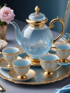 a glass tea set with gold trimmings and blue dishes on a tray next to pink flowers