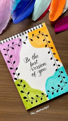 a notebook with the words be the best version of you on it next to feathers