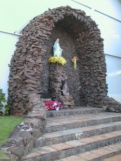 the statue is made out of rocks and has flowers in front of it on some steps