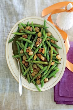 a white plate topped with green beans and nuts next to a purple napkin on top of a table