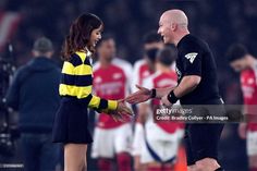 two soccer players shake hands on the field during a game with fans in the background