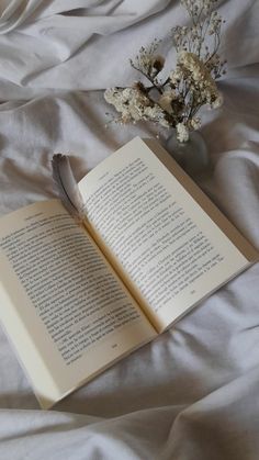 an open book with a feather resting on it next to a vase filled with flowers