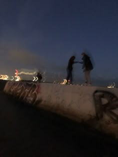 two people standing on the edge of a concrete wall with graffiti written on it at night