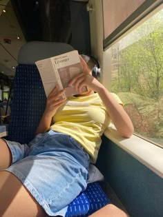 a woman reading a book while sitting in a train car with her legs up on the window sill