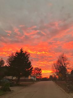 the sky is red and orange as the sun sets in the distance behind some trees