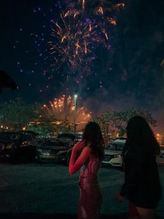 two women are looking at the fireworks in the night sky over their parking lot, while one woman holds her hand up to her ear