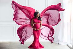 a pregnant woman wearing a pink butterfly wings costume poses for a photo in front of a white wall