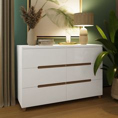 a white dresser with two drawers and a lamp on it next to a plant in a vase