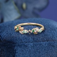 a gold ring with green and white stones on it sitting on a blue velvet cushion