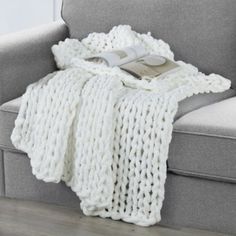 a white knitted blanket sitting on top of a gray couch next to a book