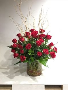 a vase filled with red roses on top of a white table next to a wall