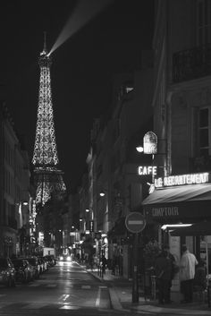 the eiffel tower is lit up at night in black and white with people walking down the street