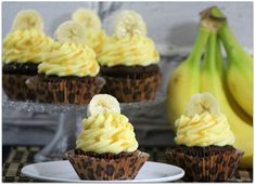 three cupcakes with banana slices and frosting sitting on a plate next to bananas