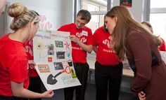 three people in red shirts are looking at a poster