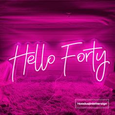 a pink neon sign that says hello forty on top of a pile of fuzzy rugs