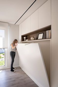 a woman standing in front of a white counter top next to a book shelf with books on it