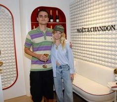 a man and woman standing next to each other in front of a wall with wine bottles