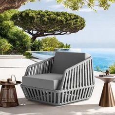 an outdoor lounge chair and side table on a patio overlooking the ocean with a tree in the foreground