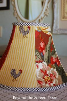 a lamp shade with roosters and flowers on the bottom is sitting on a bed