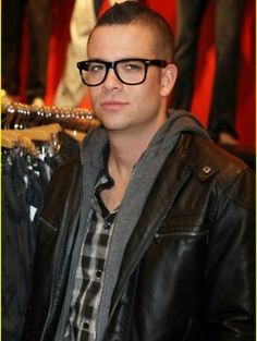 a man wearing glasses standing in front of a rack of clothes