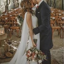 a bride and groom kissing in front of an outdoor ceremony area with rows of wooden chairs