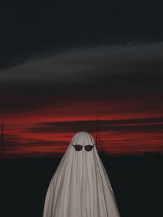 a ghost wearing sunglasses and a white cape in front of a red sky at night