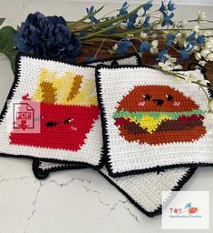 two crocheted hamburgers and fries are sitting on a table next to flowers