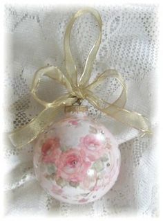 an ornament decorated with pink roses and gold ribbon on a white lace background