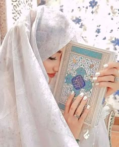 a woman in a white hijab is holding a book and looking at it