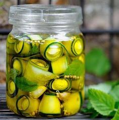 a jar filled with pickles sitting on top of a wooden table next to leaves