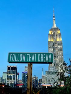 a green street sign sitting in front of a tall building with the words follow that dream on it