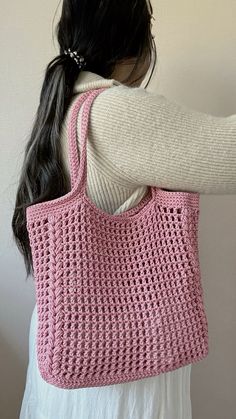 a woman is holding a pink crocheted handbag in her left arm and back