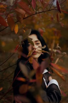 a woman standing in front of a tree with leaves on her face and hands behind her head