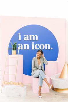 a woman sitting in front of a pink and blue sign with the words i am an icon