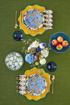 the table is set with blue and yellow plates, silverware, and fruit on it