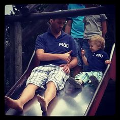 a man sitting on top of a slide next to a little boy