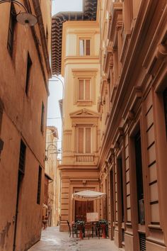 an alley way with tables and chairs in the middle, surrounded by tall brown buildings