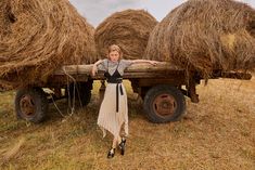 a woman is standing in front of hay bales on a farm truck with her arms outstretched