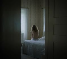 a naked woman sitting on top of a bed next to a window in a dark room