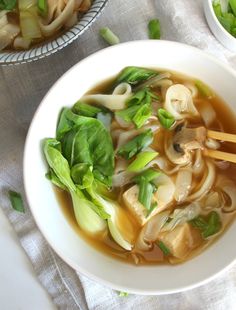 a bowl of soup with noodles, mushrooms and greens in broth on a table