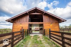 an open barn door leading to a horse stable with a wooden fence and green grass on the other side